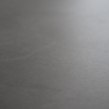 Un carreau lisse, mat et gris foncé repose à plat. sa texture de surface varie légèrement, créant des reflets subtils et lumineu