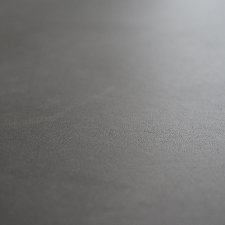 Un carreau lisse, mat et gris foncé repose à plat. sa texture de surface varie légèrement, créant des reflets subtils et lumineu