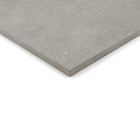 Un carreau de céramique lisse et gris repose sur une surface blanche, présentant un subtil motif moucheté. Le coin est légèremen