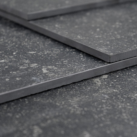 Trois carreaux gris foncé superposés, reposant sur une surface texturée, affichent un motif moucheté aux bords légèrement suréle Trois carreaux gris foncé superposés, reposant sur une surface texturée, affichent un motif moucheté aux bords légèrement suréle