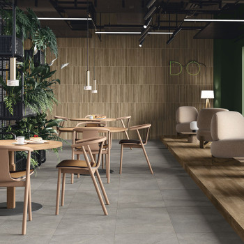 Mesas e cadeiras de madeira ficam sobre um piso de cerâmica cinza claro em um café moderno com vegetação e iluminação minimalist