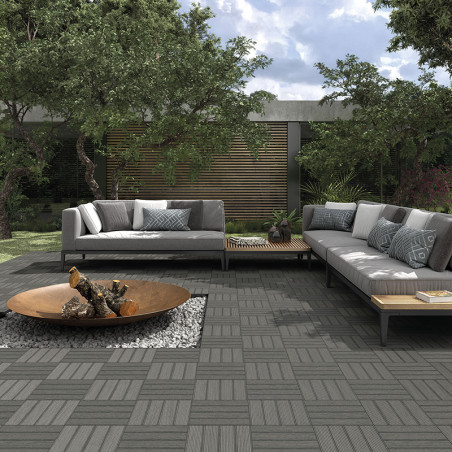 Deux canapés gris encadrent un patio extérieur moderne avec des carreaux imbriqués. Un foyer central sur gravier agrémente le ja