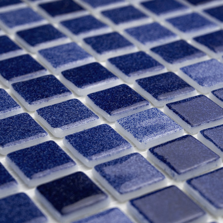 Carreaux de verre bleu disposés selon un motif en grille, réfléchissant la lumière, posés sur une base de coulis blanc.