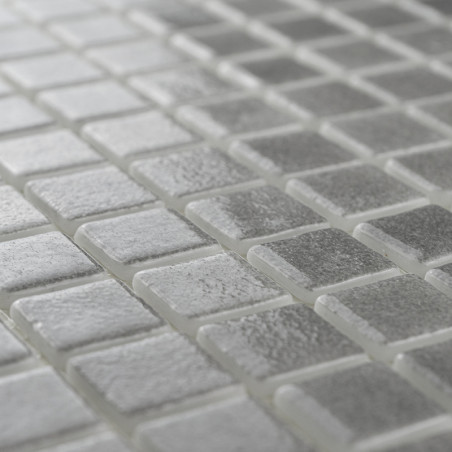 Glass tiles lie flat, reflecting light subtly, arranged in a neat grid pattern, creating a modern and sleek surface.