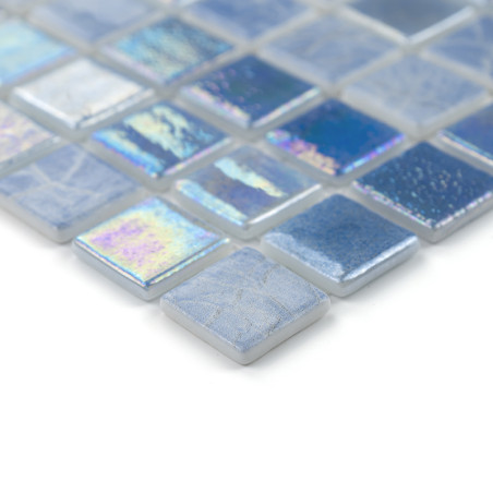 Ladrilhos de vidro quadrados refletem a luz, exibindo tons iridescentes de azul e prata, dispostos em um padrão geométrico elega