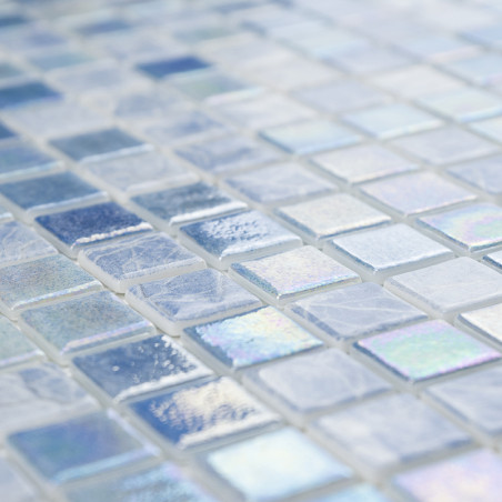Los mosaicos de vidrio iridiscentes brillan en una superficie y muestran distintos tonos de azul y blanco en un patrón de cuadrí