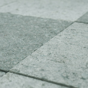 Les carreaux de pierre grise disposés en grille reposent uniformément sur le sol, formant une surface texturée et uniforme.