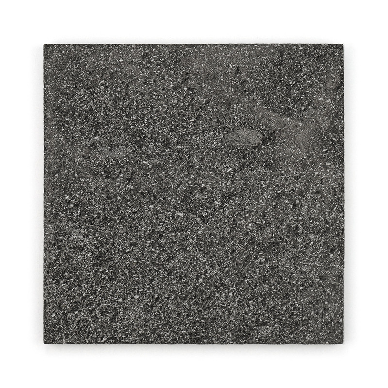 Los azulejos de piedra cuadrados muestran una textura moteada de color gris oscuro, descansando sobre un fondo blanco liso.