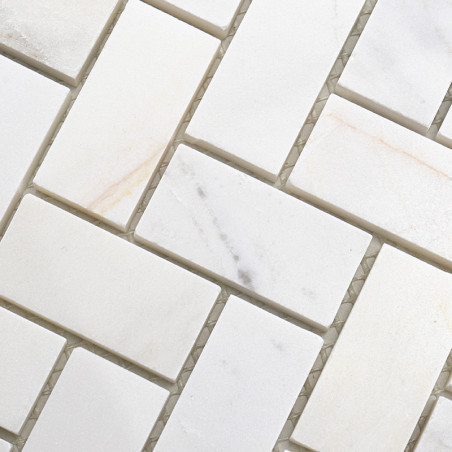 Rectangular white stone tiles arranged in a herringbone pattern, forming a textured, interlocking design on a flat surface.