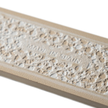 Le carreau rectangulaire présente une surface texturée en galets avec le texte « MADE IN SPAIN » au centre. une bordure beige en