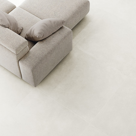 Un canapé texturé gris clair avec deux coussins repose sur un grand carrelage lisse de couleur claire, créant un décor de salon 