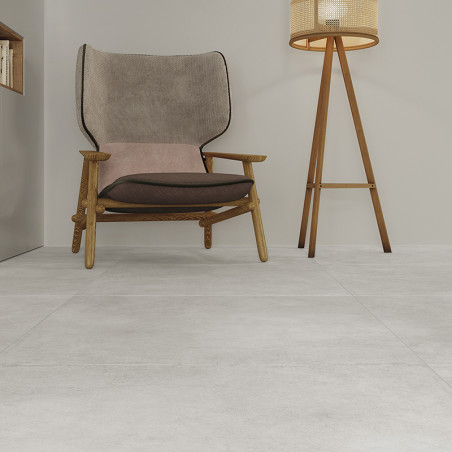Une chaise texturée repose sur un carrelage gris clair, accompagnée d'un lampadaire en bois, adossé à un mur minimaliste de coul