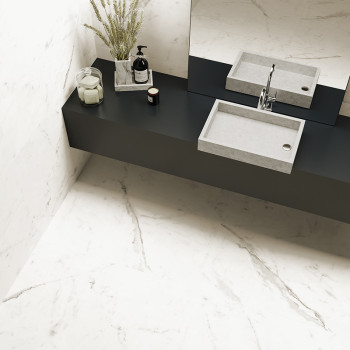 Un lavabo rectangular de hormigón se encuentra encima de una encimera negra en un baño, decorado con un jarrón, una botella y ve