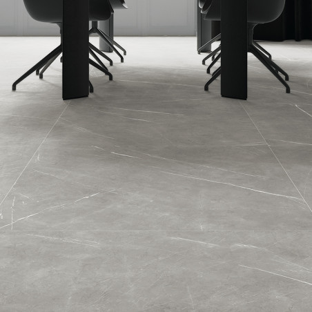 Des carreaux de marbre gris recouvrent un sol élégant et moderne sous des chaises sombres et une longue table, créant un cadre é