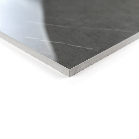 Un carreau gris foncé poli avec des motifs veinés subtils repose sur une surface blanche, reflétant une lumière douce dans un dé