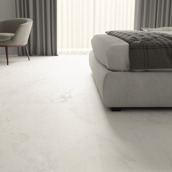 Een witte marmerachtige vloer strekt zich uit over een moderne slaapkamer, voorzien van een stoel en bed met kussens, en grijze 