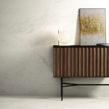 Een houten dressoir staat tegen een muur met een licht marmerpatroon. Een bolvormige lamp en abstracte kunstwerken rusten er bov
