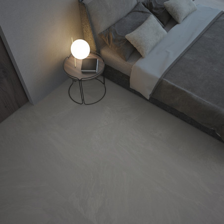Naast een modern bed ligt een gladde, grijze tegelvloer. vlakbij staat een rond bijzettafeltje met een gloeiende lamp.