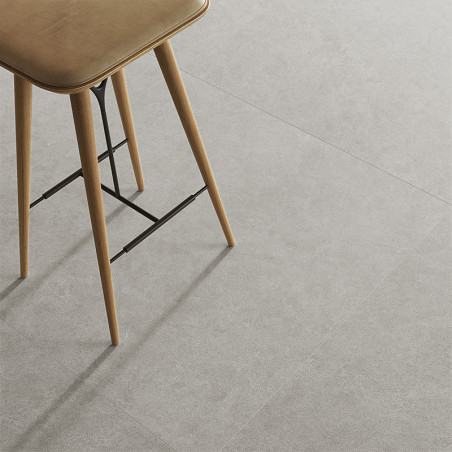 Un tabouret en bois se dresse sur un sol carrelé gris clair, ses pieds projetant des ombres, suggérant un espace intérieur minim