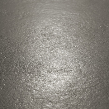 The metallic tile surface reflects light softly, displaying a slightly uneven texture in a neutral, dimly lit setting.