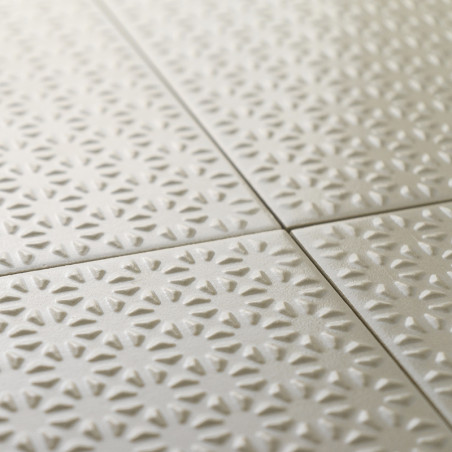 Los azulejos cerámicos texturizadas forman un patrón repetido de formas de rayos de sol en un suave color beige, dispuestas cuid