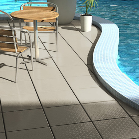 Una mesa redonda de madera con sillas de metal se asienta sobre azulejos beige junto a una piscina curva, que refleja la luz del