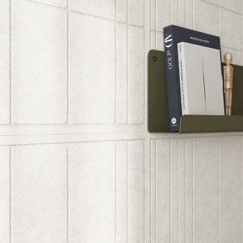 Um azulejo branco texturizado forma um padrão geométrico. Uma estante verde oliva contém livros, incluindo “art 100” e um manequ