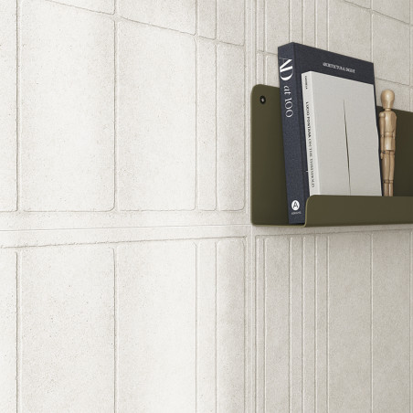 Een getextureerde witte wandtegel vormt een geometrisch patroon. Op een olijfgroene plank staan ​​boeken, waaronder art 100, en 