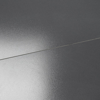 Un carreau gris foncé lisse et brillant reflète la lumière de manière subtile. Il est plat, divisé par une ligne de coulis droit