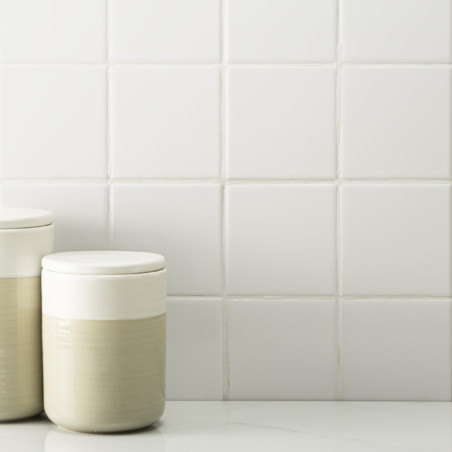 Dos tarros de cerámica de color crema descansan sobre una superficie lisa sobre un fondo de azulejos blancos uniformes. Dos tarros de cerámica de color crema descansan sobre una superficie lisa sobre un fondo de azulejos blancos uniformes.
