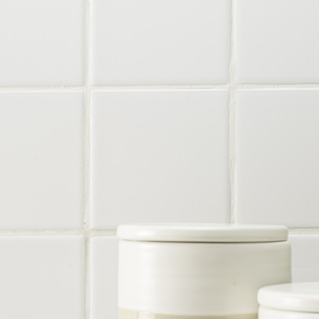 Dos frascos de cerámica blanca con tapa se asientan sobre un fondo de azulejos cuadrados blancos con líneas de lechada visibles. Dos frascos de cerámica blanca con tapa se asientan sobre un fondo de azulejos cuadrados blancos con líneas de lechada visibles.