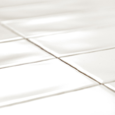 Los azulejos rectangulares blancos están dispuestos en forma de cuadrícula, proyectando sombras suaves debido al reflejo de la l