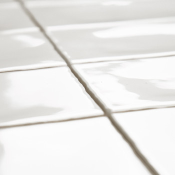 Los azulejos de cerámica blancos se encuentran perfectamente en un patrón de cuadrícula, con reflejos de luz que crean sutiles r