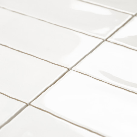 Los azulejos rectangulares blancos están alineados en un patrón escalonado, reflejando la luz sobre una superficie lisa y brilla