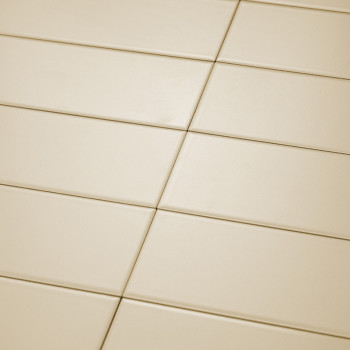 Ladrilhos retangulares de cor creme estão bem organizados em um padrão de grade diagonal. A superfície lisa reflete a luz unifor