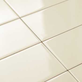 Os ladrilhos cerâmicos de cor creme são dispostos em um padrão de grade, refletindo a luz suavemente em um piso liso e polido.