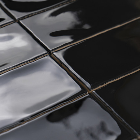 Les carreaux de céramique noirs brillants réfléchissent la lumière, disposés uniformément selon un motif en grille. Des reflets 