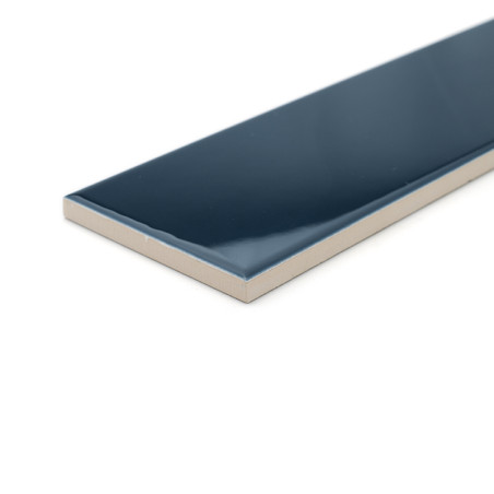 Un azulejo cerámico rectangular de color azul oscuro brillante se encuentra aislada sobre una superficie blanca, mostrando su ac