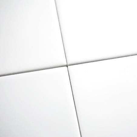 Cuatro azulejos de cerámica blancas y lisas forman una cuadrícula ordenada, que se cruza en sus esquinas, creando un patrón simé