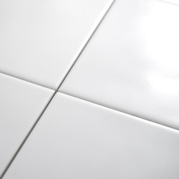 Quatro ladrilhos de cerâmica brancos brilhantes se cruzam, formando um padrão de grade em uma superfície lisa, refletindo a luz 