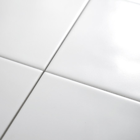 Cuatro azulejos de cerámica blanca brillante se cruzan, formando un patrón de cuadrícula sobre una superficie lisa, reflejando l