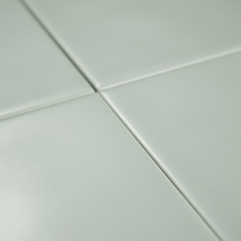 Cuatro azulejos de color verde claro se unen en las esquinas formando una cuadrícula, creando una superficie lisa y limpia con s