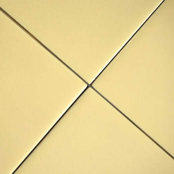 Cuatro azulejos lisos, cuadrados y de color amarillo pálido se unen en el centro, formando un patrón de cruz simétrico. cada los