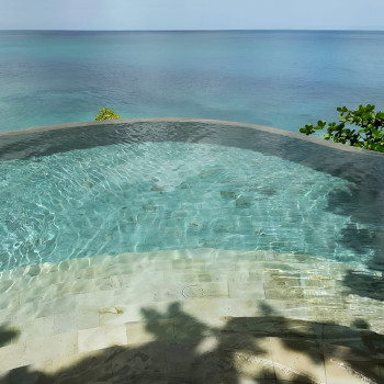 Uma grade de ladrilhos de pedra turquesa margeia uma piscina reflexiva ao lado de um deck de madeira texturizado.