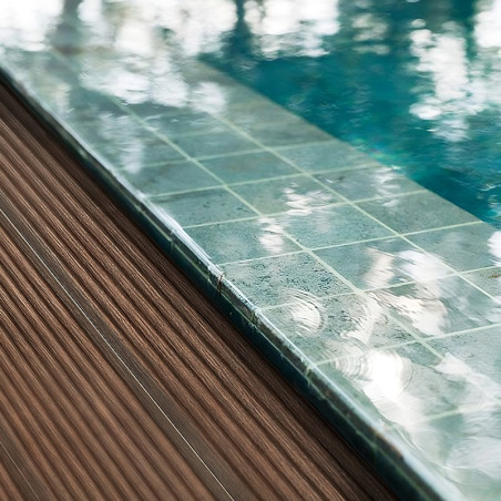 Une grille de carreaux de pierre turquoise borde une piscine réfléchissante à côté d’une terrasse en bois texturée.