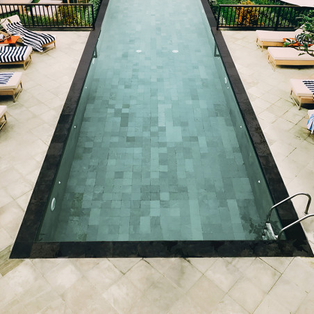 Los azulejos de piedra rectangulares forman el fondo de una piscina bajo agua clara, rodeada de tumbonas y plantas verdes vibran