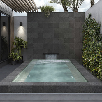 Des carreaux de pierre sombre forment un mur d'eau, avec de l'eau tombant en cascade dans une petite piscine rectangulaire. ento