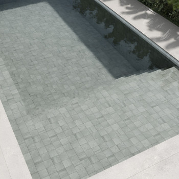 Los azulejos de piedra de color gris claro forman el suelo de una piscina sumergida, que refleja la luz del sol, rodeada de bord
