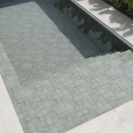 Hellgraue Steinfliesen bilden einen unter Wasser liegenden Poolboden, der das Sonnenlicht reflektiert und von Betonrändern und g