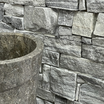 Revestimentos de pedra cobrem o exterior de um edifício moderno, cercado por um caminho de concreto e gramado verde.